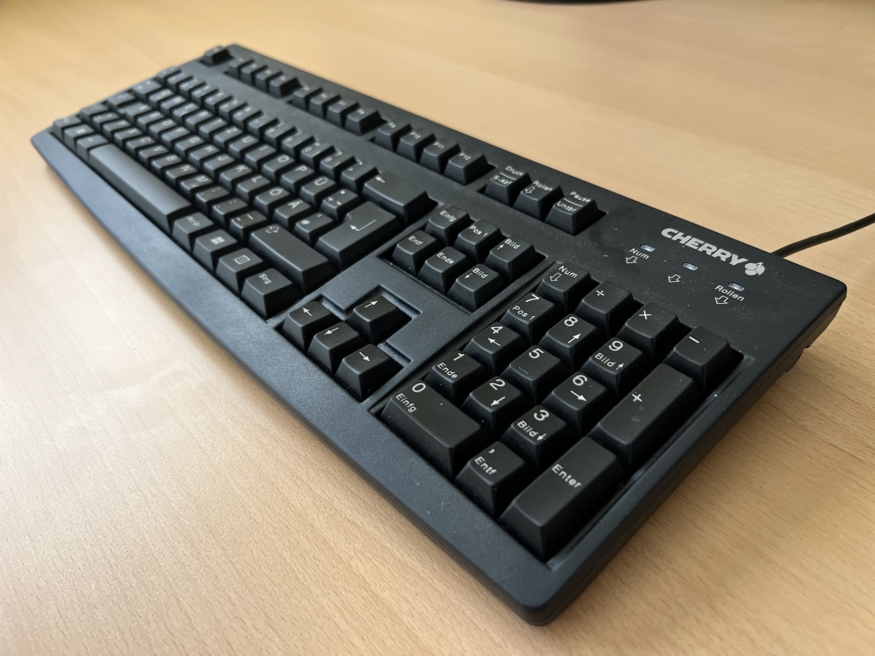 Eine schwarze Cherry-Tastatur ist auf einer Holzoberfläche platziert und verfügt über einen Ziffernblock sowie ein Standard-Tastenlayout.